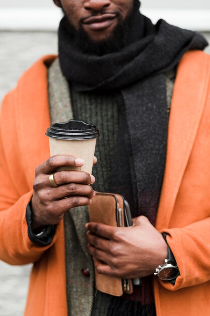 コーヒーのカップを保持しているオレンジ色のコートの男