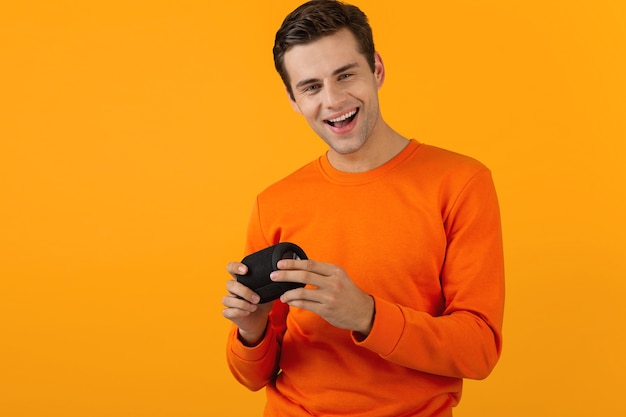  man in orange sweater holding wireless speaker happy listening to music having fun isolated on yellow