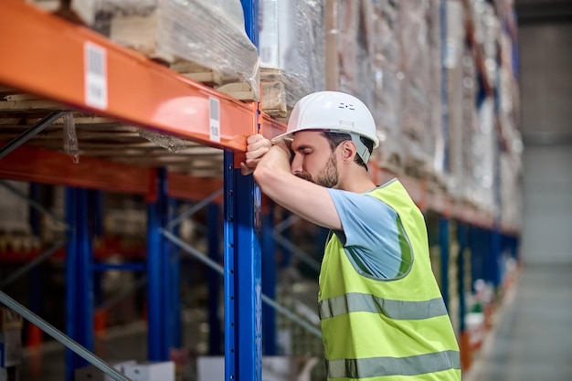 Man in overalls resting leaning against warehouse rack