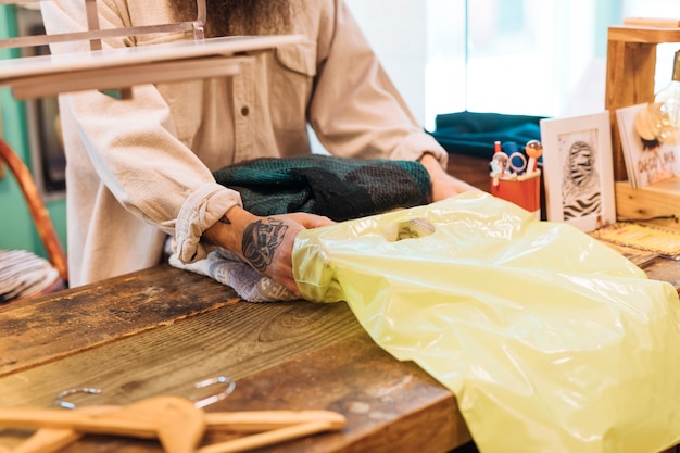 Uomo proprietario al bancone di imballaggio i vestiti in sacchetto di plastica gialla