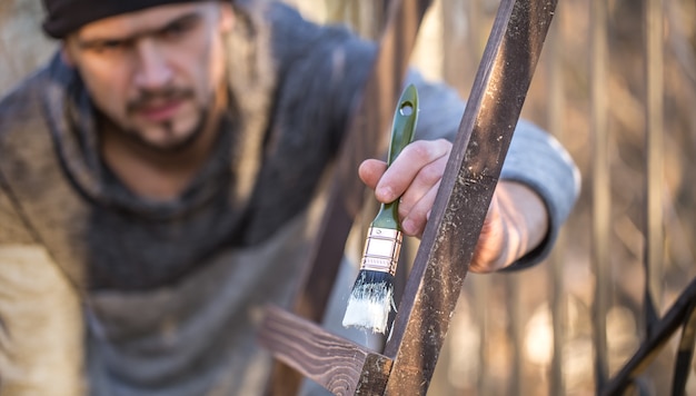 A man paints with white paint on wooden planks. Man in industrial concept. There is a place for text, the object is close up.