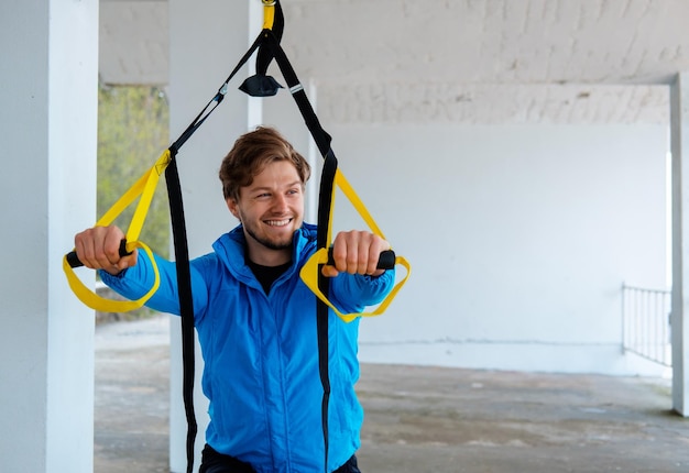 Free photo a man in a park improving his legs flexibility with fitness trx strips.