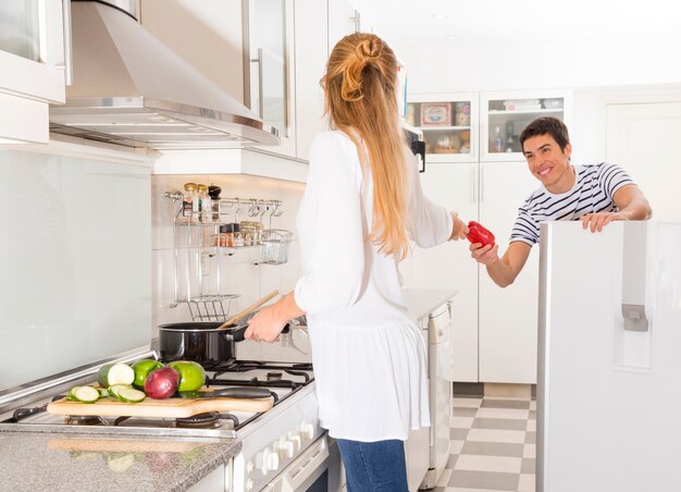 Man passing vegetable to her wife preparing food in the kitchen