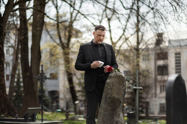 Free photo man paying respect to a tombstone at the cemetery