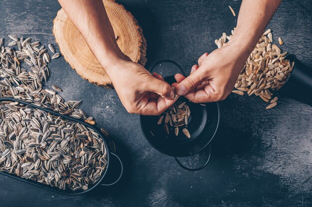 Man peeling off sunflower seed on a black background. top view.