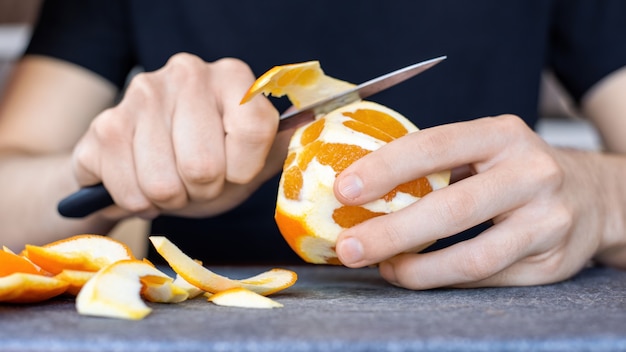 요리판에 칼을 사용하여 오렌지 껍질을 벗기는 남자