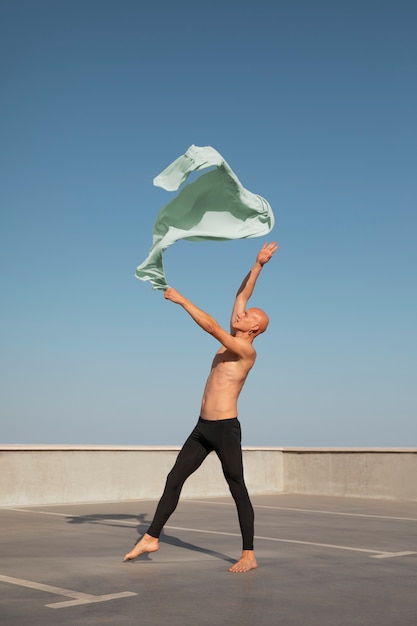 Бесплатное фото Мужчина исполняет артистический танец на крыше с голубым небом