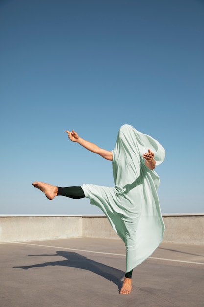 Free photo man performing artistic dance on a rooftop with blue sky