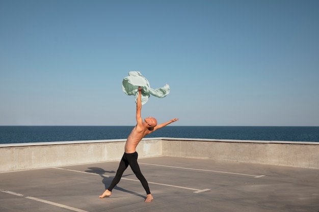 Мужчина исполняет артистический танец на крыше с голубым небом