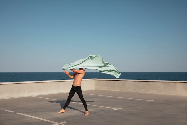 Foto gratuita uomo che esegue una danza artistica su un tetto con cielo blu