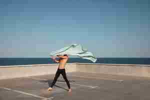 Foto gratuita uomo che esegue una danza artistica su un tetto con cielo blu