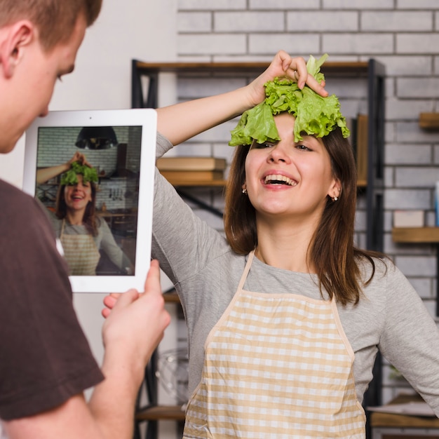 Man photographing woman with salad leaf on head