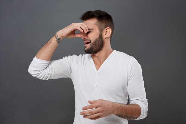 Man pinches nose because of bad smell over grey wall