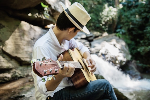 Man play guitar near to the waterfall 