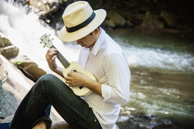 Man play ukulele new to the waterfall 