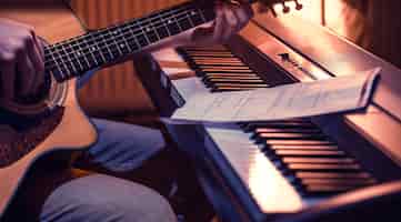 Foto gratuita uomo che suona la chitarra acustica e il piano in primo piano, note di registrazione, bel colore di sfondo, concetto di attività musicale