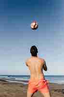 Free photo man playing football at the beach