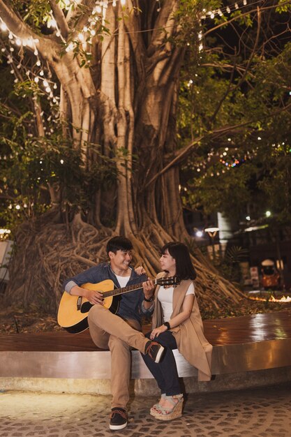 Человек играет на гитаре для своей подруги под деревом