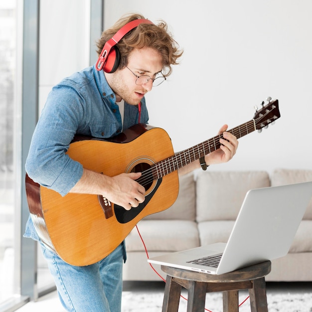 Free photo man playing guitar and looking at laptop