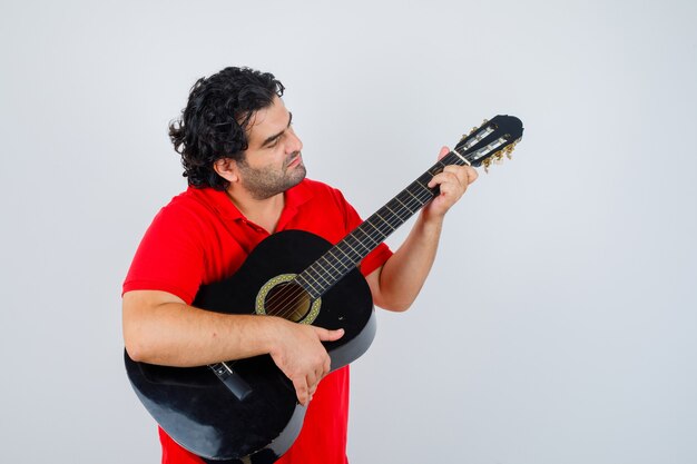 man playing guitar in red t-shirt and looking focused