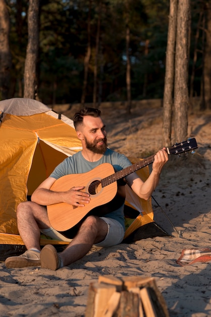 Free photo man playing guitar next to tent