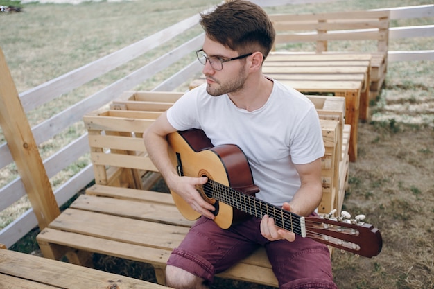 Man playing guitar on wooden tables with glasses to see