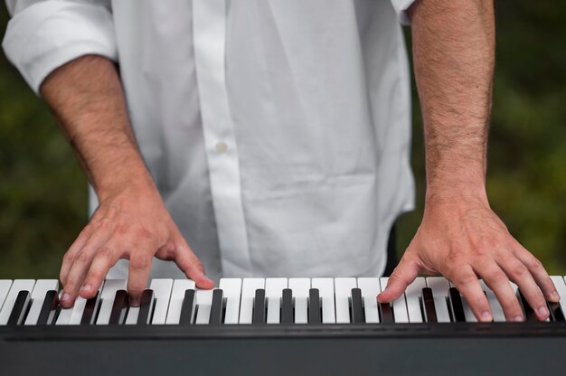 屋外でクローズアップシンセサイザーキーボードを演奏する男