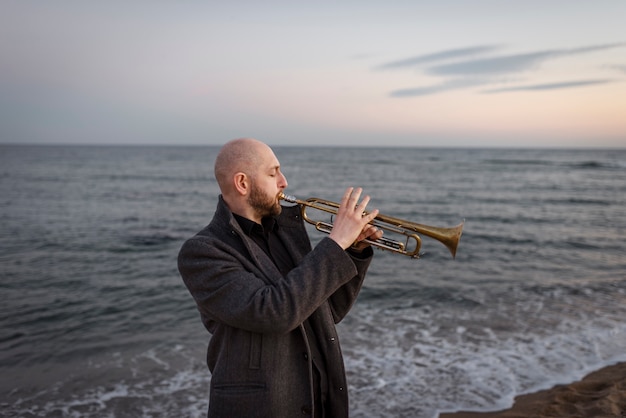 Man playing trumpet at seaside medium shot