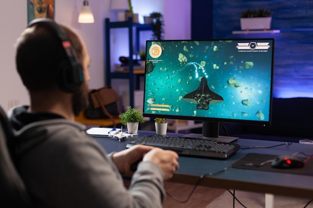 컴퓨터에서 컨트롤러와 헤드폰으로 비디오 게임을 하는 남자. 온라인 게임을 위해 조이스틱과 오디오 헤드셋을 사용하는 플레이어. 게임을 할 수 있는 장비로 재미있는 활동을 하는 게이머.