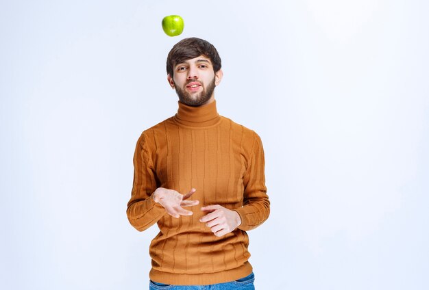 Man playing with a green apple and throwing it up.