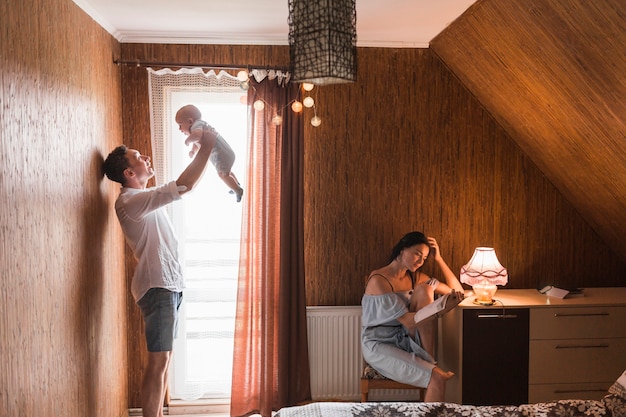 아내가 집에서 책을 읽는 동안 그의 아기와 함께 노는 남자