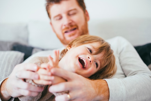 Man playing with laughing son on sofa