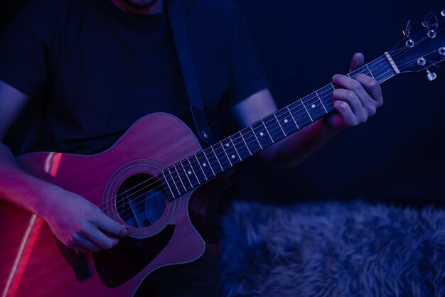 男は暗い部屋のコピースペースでアコースティックギターを弾きます。ライブパフォーマンス、アコースティックコンサート。