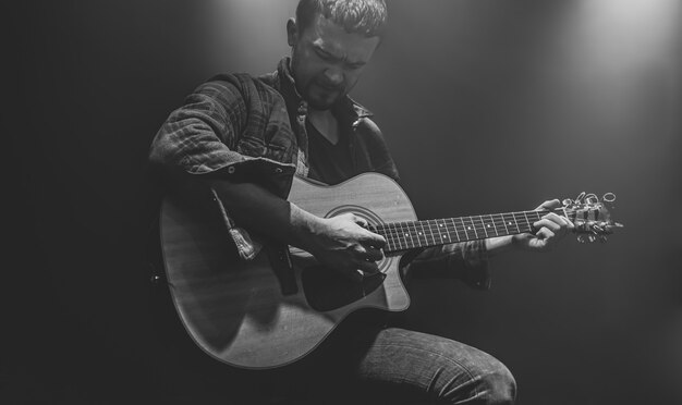 A man plays an acoustic guitar at a partially lit concert.