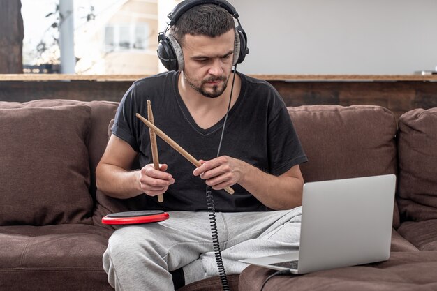 Мужчина играет в барабан и смотрит на экран ноутбука. Концепция онлайн-уроков музыки, уроков по видеоконференцсвязи.