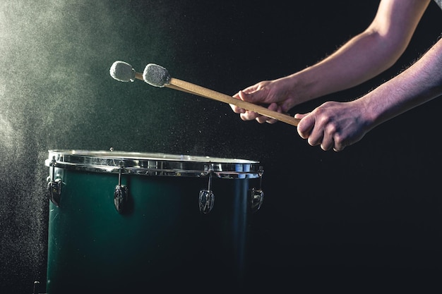 Un uomo suona uno strumento musicale a percussione con bastoncini su uno sfondo scuro