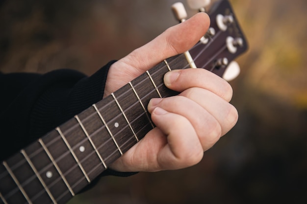 男は自然のクローズ アップ指でウクレレ ギターを弾く弦をクランプします。