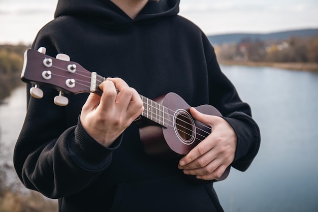 Un uomo suona la chitarra ukulele in primo piano della natura