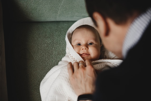 Man plays with a little newborn baby enveloped in soft blanket