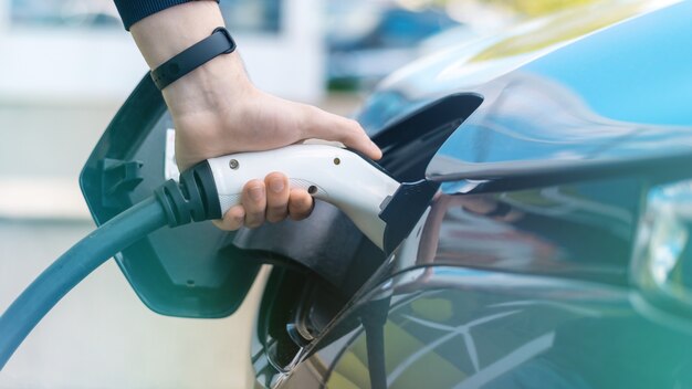 Man plugging in charger into an electric car at charge station