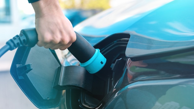 Free photo man plugging in charger into an electric car at charge station