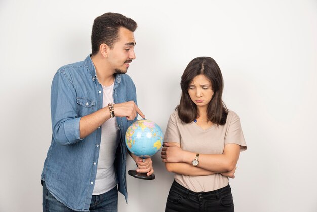 Man pointing at earth globe next to resentful girl.