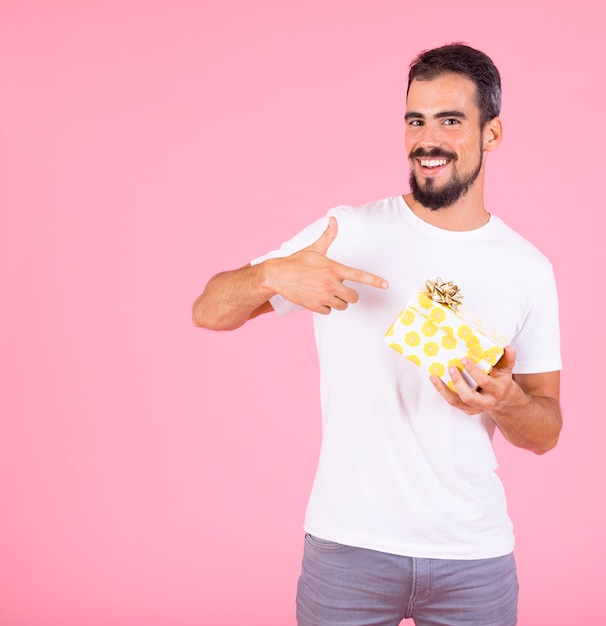 Man pointing finger on gift box with golden bow against pink backdrop