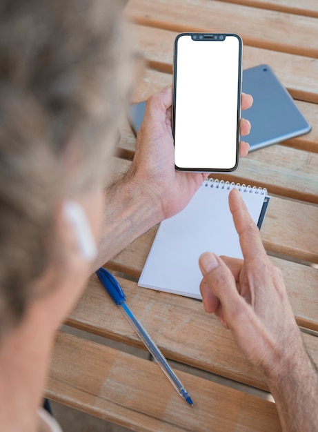 Man pointing finger toward mobile phone with blank white screen on wooden table