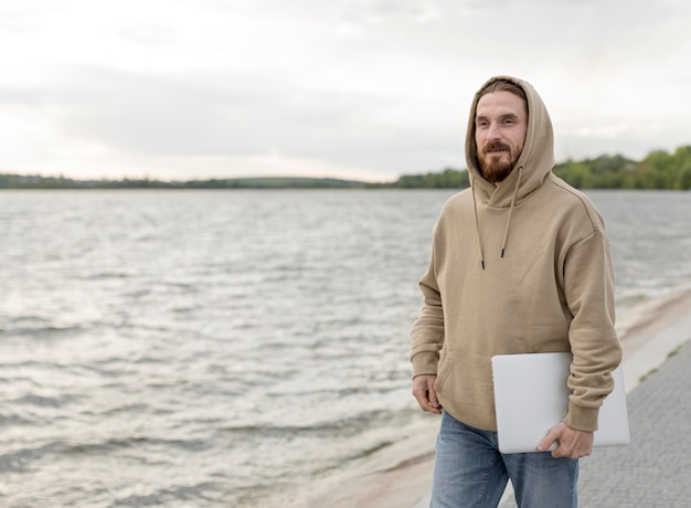 Man posing next to lake while carrying laptop