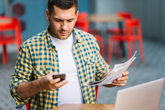 Man posing with phone and newspaper