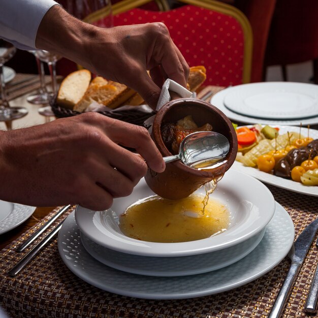 木製のテーブルのプレートに肉とおいしい東部エンドウ豆のスープを注ぐ男。ハイアングル。