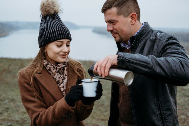 屋外の女性のカップに温かい飲み物を注ぐ男