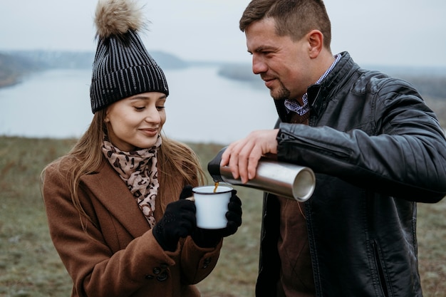 Man pouring hot drink in woman's cup outdoors