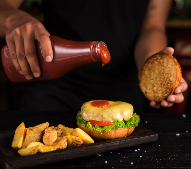 おいしいビーフバーガーにケチャップを注ぐ男